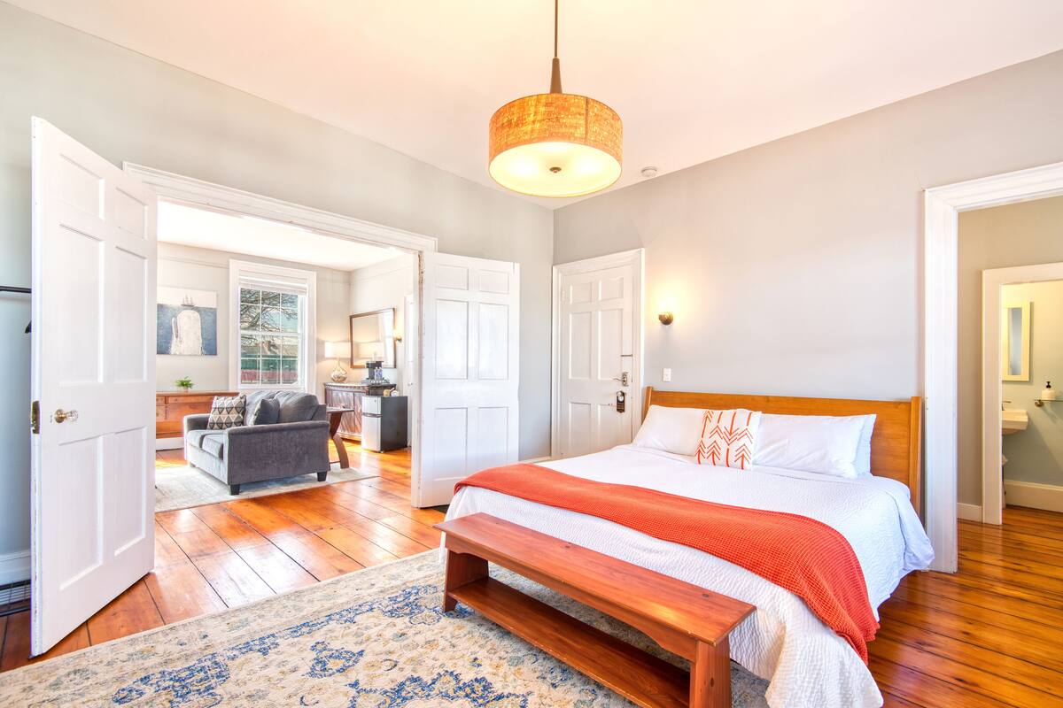 A bedroom with a wooden bed, a bench, a rug, and a hanging light fixture.