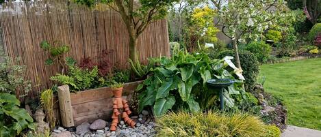 Un jardín con una mesa de madera, una cerca de bambú y diversas plantas.