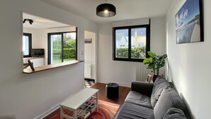 A modern living room with a grey sofa, a white coffee table, a large mirror, and a view of the outdoors through a window. - Maison Les Pieds Dans Leau Large vue sur mer 20 m de la Plage Wide Sea View (Loctudy)