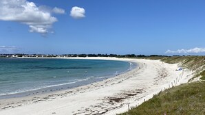A coastal beach with a clear sky, sandy shore, and a distant shoreline with buildings. - Maison Les Pieds Dans Leau Large vue sur mer 20 m de la Plage Wide Sea View (Loctudy)