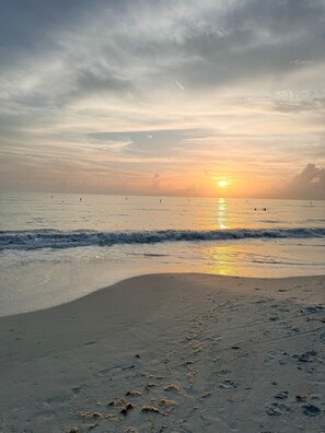 Une plage au coucher du soleil, avec des vagues et des empreintes de pas dans le sable.