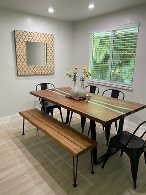 Een eetgedeelte met een houten tafel, zwarte stoelen, een bank en een vaas met gele bloemen.