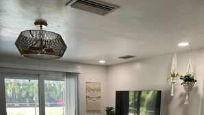 Een moderne woonkamer met een flatscreen-tv, rieten meubels en uitzicht op een zwembad door grote schuifdeuren.