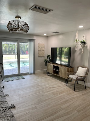 A modern living room with a flat-screen TV, wicker furniture, and a view of a pool through large sliding doors. - Updated Tropical Oasis, Very Private, Book now for Family Vacations (Bonita Springs)
