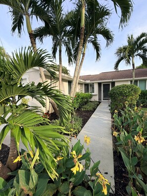 Une propriété résidentielle avec un chemin menant à une maison, entourée de palmiers et de plantes à fleurs.