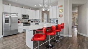 Una cocina moderna con armarios blancos, electrodomésticos de acero inoxidable y una isla central con taburetes rojos.