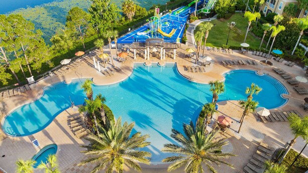 Zona de piscina en un complejo turístico, con varias piscinas, sillas de descanso y palmeras.