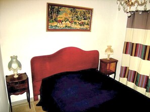 A bedroom with a red headboard, a painting of a tropical scene, a striped curtain, and two bedside tables with lamps. - Maison "marianne" Avec Court Intèrieure (Ferrals-les-Corbières)