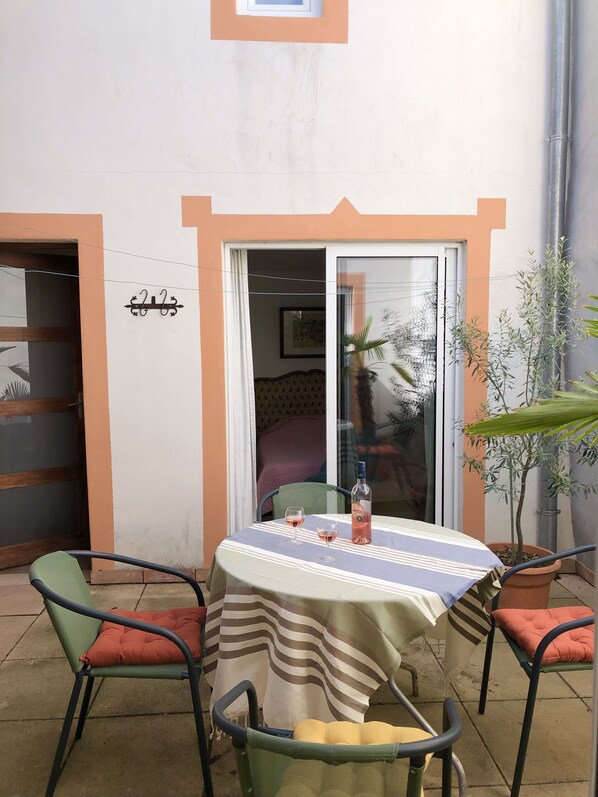 A patio area with a table set for two, two chairs, a bottle of wine, and a potted plant. - Maison "marianne" Avec Court Intèrieure (Ferrals-les-Corbières)