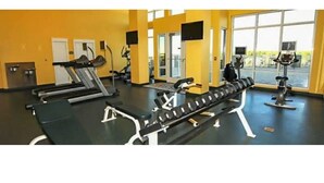 Un gimnasio con equipo de ejercicio, ventanas amplias y suelo negro.