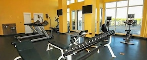 Ein Fitnessstudio mit Trainingsgeräten, großen Fenstern und einem schwarzen Boden.