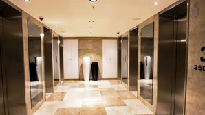 Un hall d’ascenseur moderne avec un sol en marbre poli, des murs recouverts de miroirs et un grand vase blanc placé au centre.