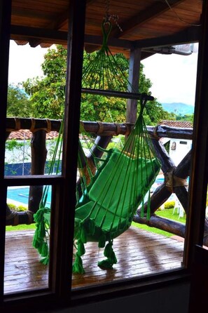 Relax in a hammock suspended from the ceiling, overlooking a serene pool and lush surroundings.