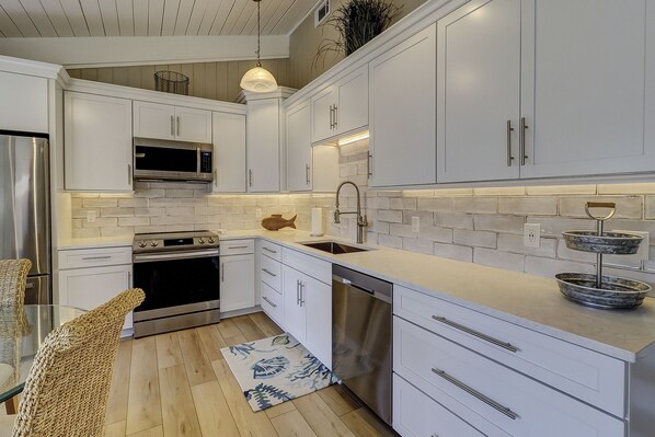 Une cuisine moderne avec des meubles blancs, des appareils électroménagers en acier inoxydable et un plancher en bois.