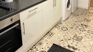 A compact kitchen with a stove, kettle, sink, and washing machine. - Modern 1 Bedroom Flat in St Helens – Ideal for Relocation or Work Trips (St Helens)