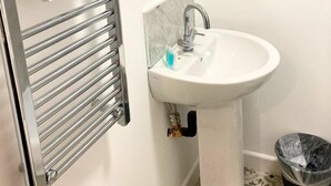 A bathroom with a white sink, a towel rack with a towel, a mirror, and a trash bin. - Modern 1 Bedroom Flat in St Helens – Ideal for Relocation or Work Trips (St Helens)