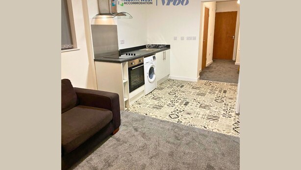 Ein gemütlicher Wohnraum mit Küchenzeile, Waschmaschine, Sofa und einem gemusterten Teppich.