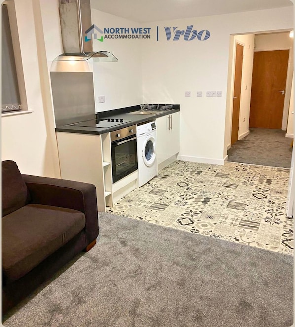 A compact living space with a kitchenette, a washing machine, a sofa, and a patterned carpet.