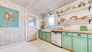 Une cuisine avec des meubles de couleur verte, un plan de travail blanc et une fenêtre au-dessus de l’évier.
