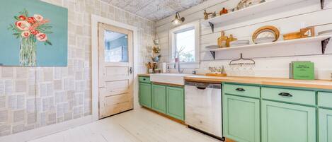 A kitchen with green cabinets, a white countertop, and a window above the sink.