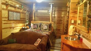 A cozy log cabin room with a bed, a wooden bench, a sink, and a mirror. - Mountain Peaks Inn, OLD BALDY MTN SUITE, Downtown Hill City (Hill City)
