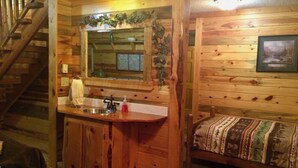 A wooden cabin interior with a kitchen area, a bed with patterned bedding, and a staircase. - Mountain Peaks Inn, OLD BALDY MTN SUITE, Downtown Hill City (Hill City)