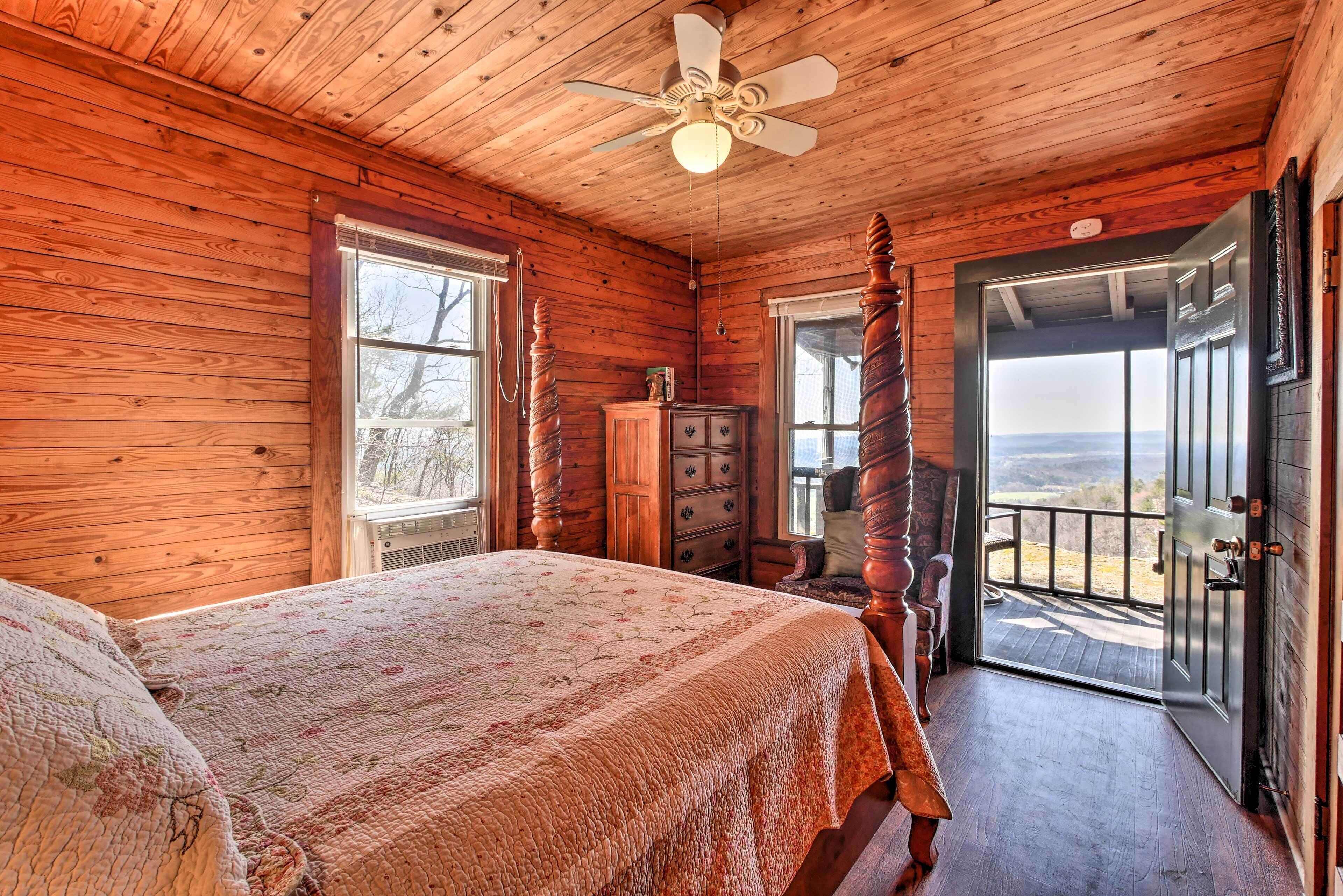 A wooden cabin bedroom with a four-poster bed, a ceiling fan, and a view through the door.