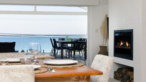 A dining area with a table set for two, a fireplace, and a view of the sea.