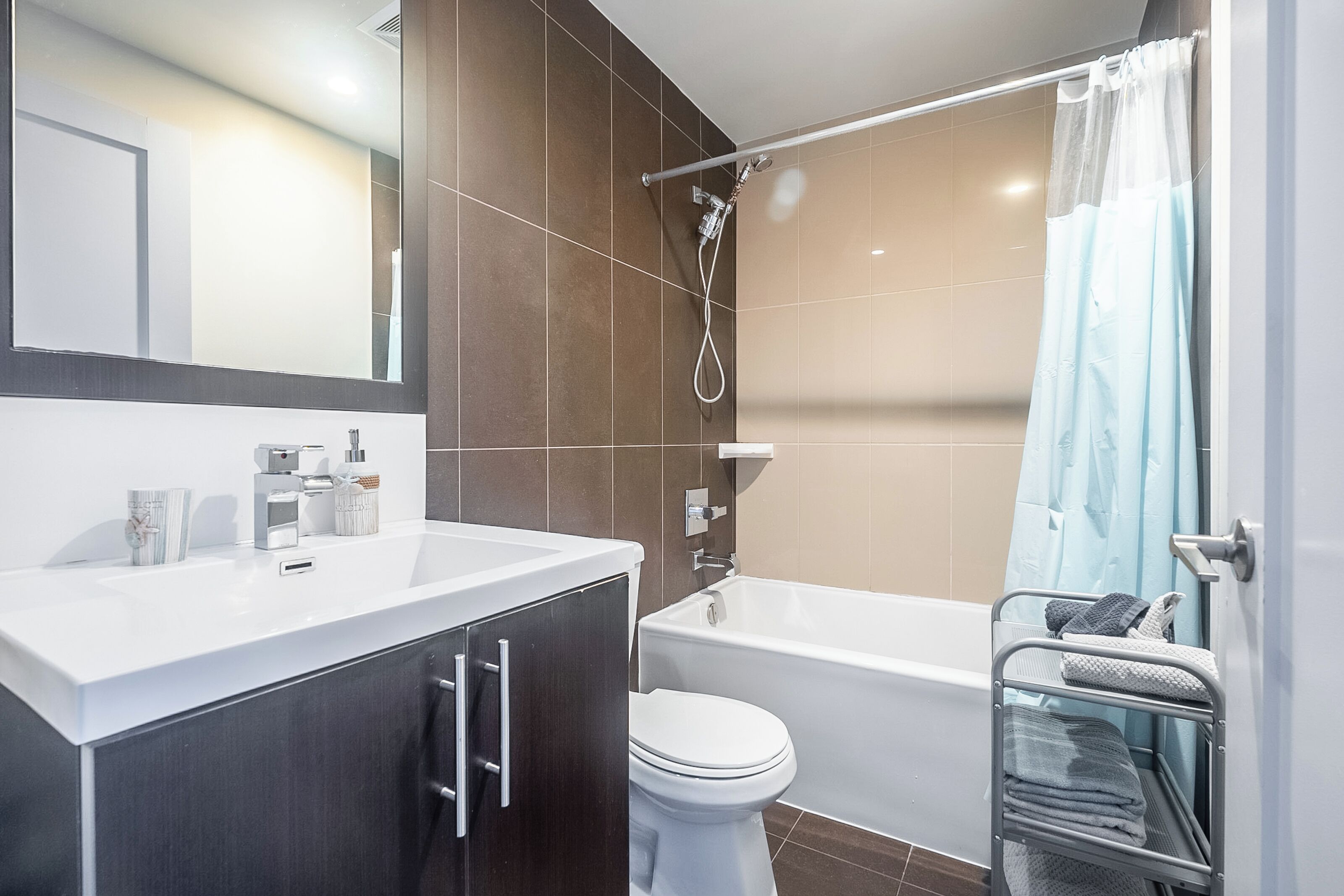 Un bagno moderno con un lavandino bianco, mobili scuri, un WC bianco, una vasca da bagno e una doccia.