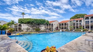 A swimming pool with a clear blue sky, palm trees, and a building with a red roof in the background.