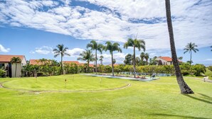 A well-maintained lawn with a pool, palm trees, and buildings with red roofs.