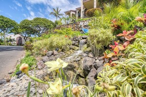 Uma área ajardinada com uma cascata, plantas tropicais e um edifício com uma placa que diz 'Maui'.