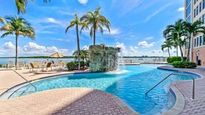 A pool area with a clear view of the water, lounge chairs, palm trees, and a building in the background. - Lovers Key Resort 401 (Fort Myers Beach)