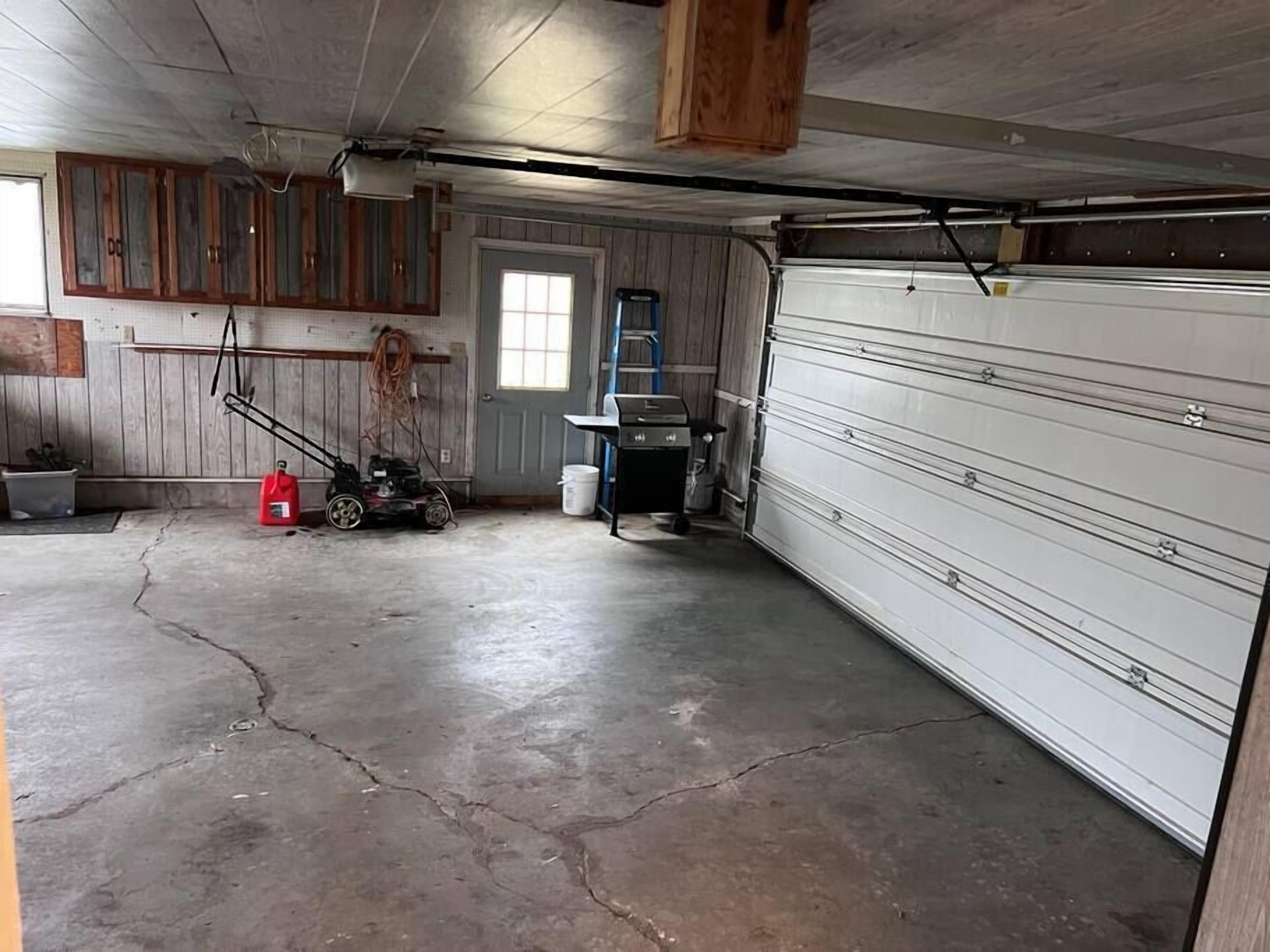 Un garage con pavimento in cemento, armadietti in legno, una porta e un basculante.