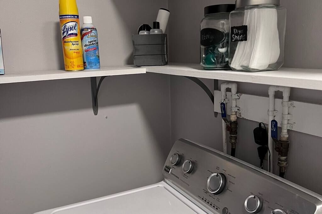 A laundry area with a washing machine, detergent bottles, and cleaning supplies on shelves.