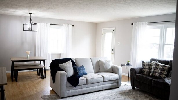 A living room with a grey sofa, a dark sofa, a wooden dining table with a vase, and a hanging light fixture. - Soldiers Home (West Lafayette)