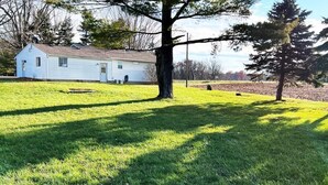 A single-story white house with a garage, surrounded by a well-maintained lawn and a large tree. - Soldiers Home (West Lafayette)