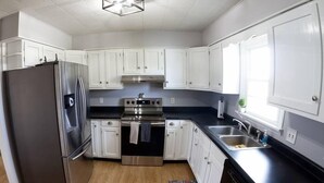 A modern kitchen with white cabinets, stainless steel appliances, and a black countertop. - Soldiers Home (West Lafayette)