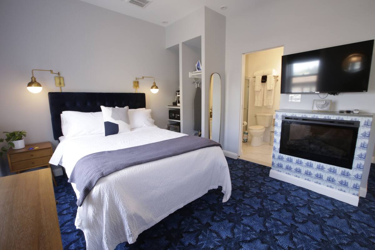 A hotel room with a large bed, a television mounted on the wall, and a fireplace.