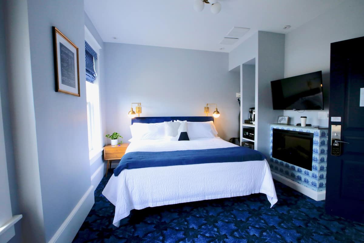 A hotel room with a large bed, bedside lamps, a flat-screen TV, a small table with a plant, and a door with a keycard lock.