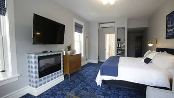Una camera da letto con un letto, una TV montata sopra un caminetto decorato, un comò e uno specchio.
