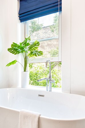 A bathroom with a white bathtub, a window with blue curtains, and a potted plant. - Hudson Whaler (Hudson)