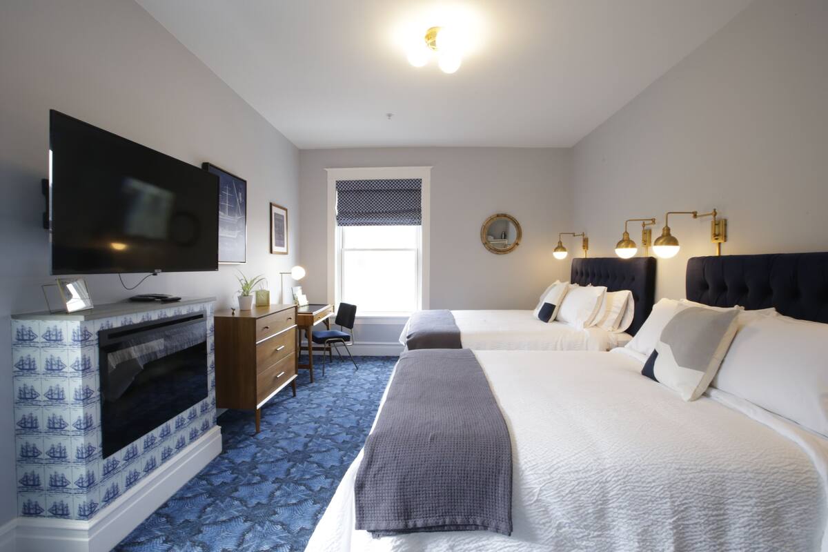 A hotel room with a flat-screen TV, a fireplace, a desk with a chair, two beds, and a window with blinds.