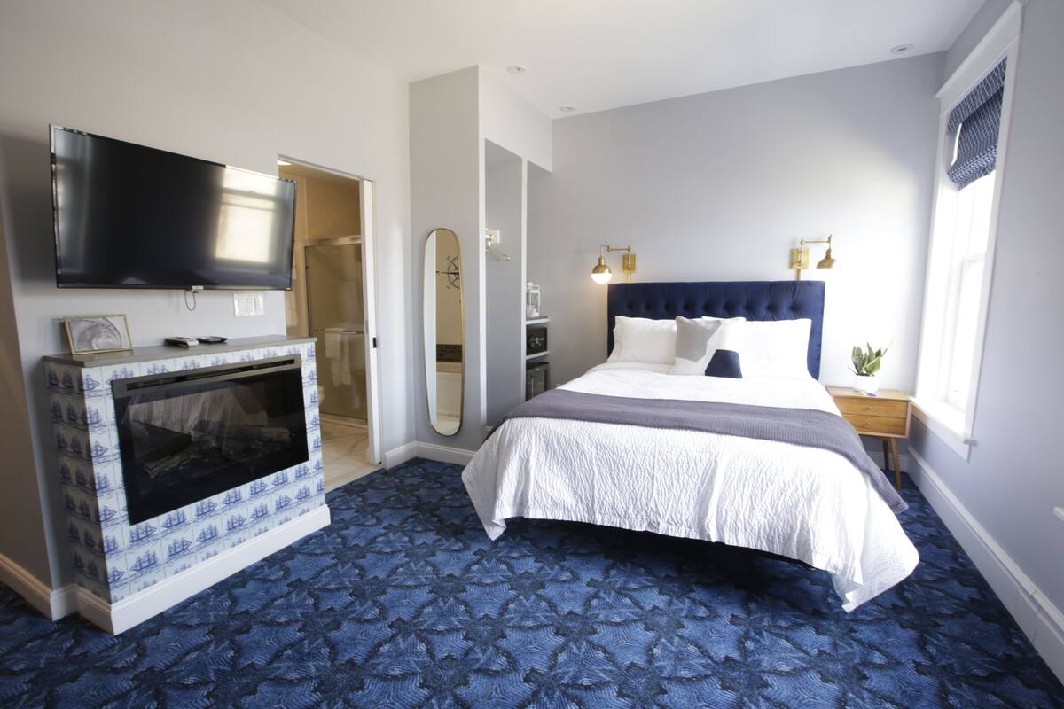 A hotel room with a large bed, a flat-screen TV, a mirror, and a small table with a plant.