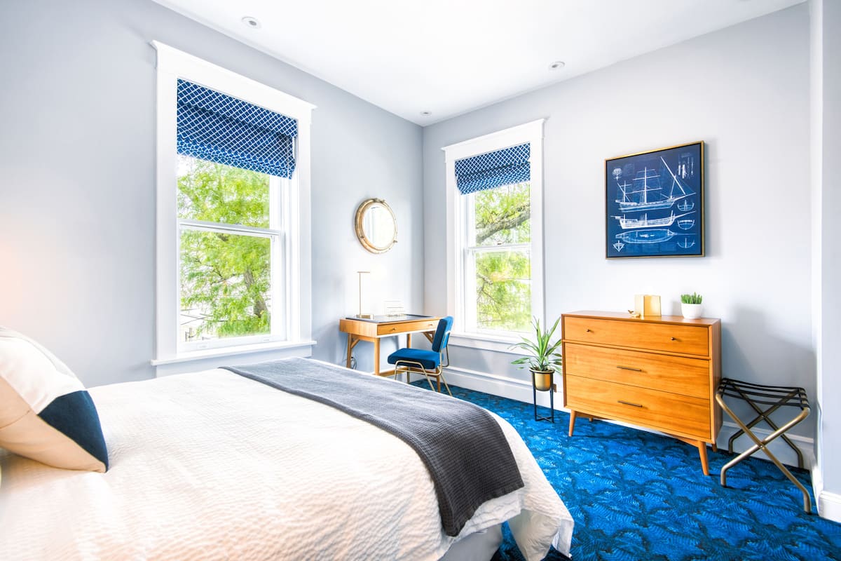 A bedroom with a bed, a desk, a dresser, and a window with a view of trees.