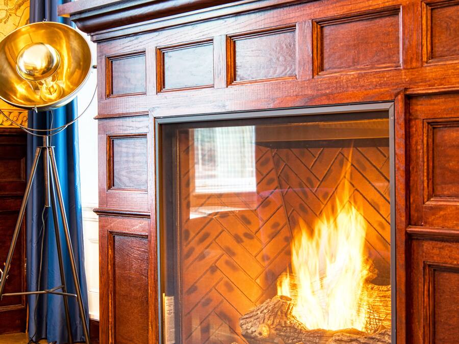 A fireplace with a ship model above it, a brass floor lamp, and a patterned rug on the floor.