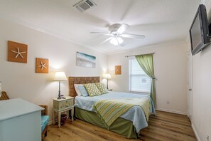 Ein Schlafzimmer mit einem Bett, Nachttischen, einem Deckenventilator, einem Fenster mit Vorhängen und Wanddekorationen, darunter Seesterne.