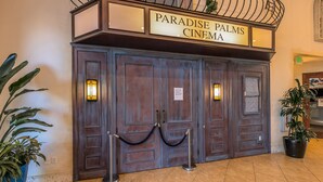 Une entrée de cinéma en bois, avec une enseigne indiquant « Paradise Palms Cinema », comprenant une double porte et deux lampes fixées aux murs.