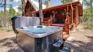 Eine Holzhütte mit Whirlpool, einer Holzterrasse und einer überdachten Veranda.