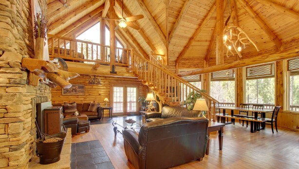 Ein geräumiges Holzhaus-Interieur mit Kamin aus Stein, Ledermöbeln, einem Essbereich und großen Fenstern.